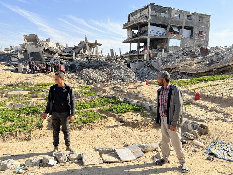 Nabil Azab (R) stands near the greens his family is tending. Behind are the remains of the apartment building his family still lives in - despite the danger. WFP/Jonathan Dumont